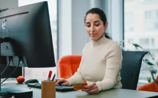 Woman checking her card while completing a task on her computer, in an office